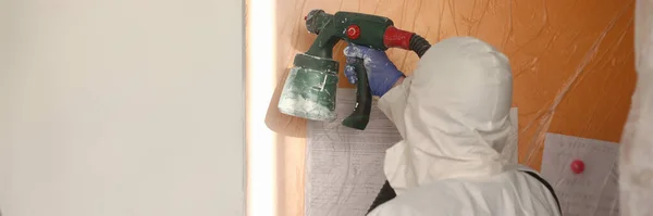 Constructeur masculin en uniforme, peinture au pistolet pulvérisateur sur mur — Photo