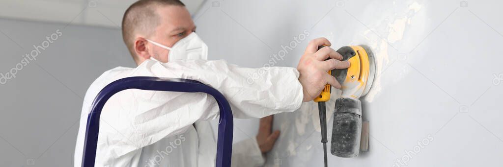 Male builder in uniform cleans wall with putty