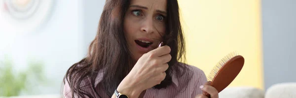 Frightened woman holds comb in her hands and looks at her hai — Stock Photo, Image