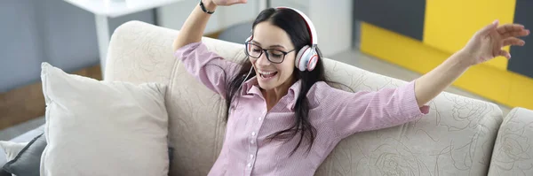 Mulher em fones de ouvido senta-se no sofá com laptop e ri. — Fotografia de Stock