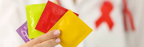 Infektionssjukdomsläkare med rött band på uniform håller många kondomer i handen närbild — Stockfoto
