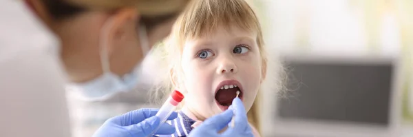 Lekarz bierze materiał biologiczny od małej dziewczynki z kijem w ustach.. — Zdjęcie stockowe