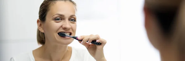 Mujer con una camiseta blanca se cepilla los dientes delante del espejo — Foto de Stock