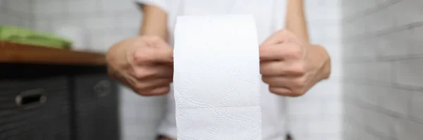 Woman sits on toilet and holds toilet paper in her hands. — Stock Photo, Image