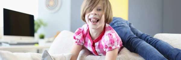 Cheerful girl lie on back of sofa and show her tongue. — Stock Photo, Image