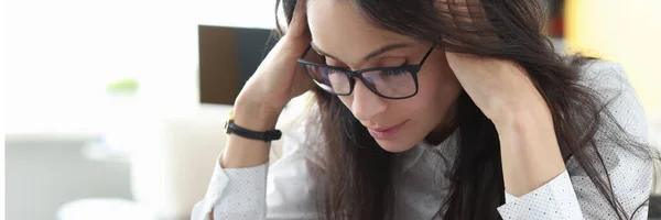 Fáradt nő szemüveggel ül az asztalnál és masszírozza a fejét a kezével és gondolkodik.. — Stock Fotó
