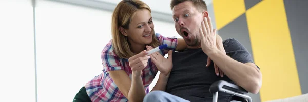 Здивований чоловік в інвалідному візку і радісна жінка дивляться тест на вагітність . — стокове фото