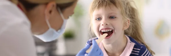 Kinderärztin in Schutzmaske und Gummihandschuhen untersucht Kehle des kleinen Mädchens — Stockfoto