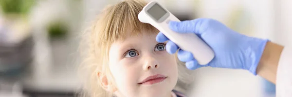 Médecin pédiatre en gant de caoutchouc mesure la température de l'enfant avec thermomètre infrarouge portrait — Photo