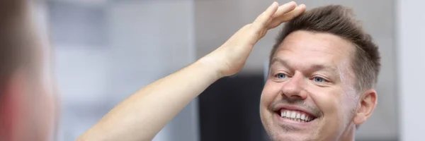 Jongeman kijkt in de spiegel en straalt zijn haar met zijn hand — Stockfoto