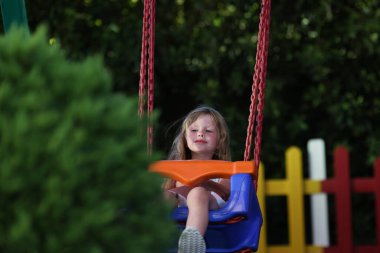 Küçük kız plastiğe biniyor. Zincirlerle parkta sallanıyor..