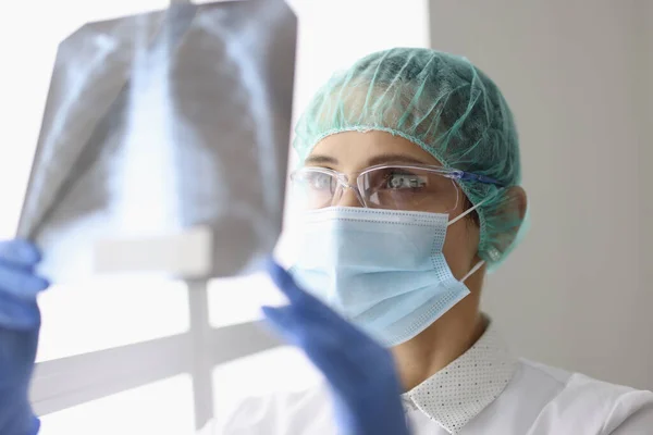 Lékař v rukavicích a ochranné masce vyšetřuje rentgen plic s pneumonií pacienta s covid19. — Stock fotografie