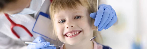 Médico dentista examina dentes de pequena menina sorridente na clínica — Fotografia de Stock