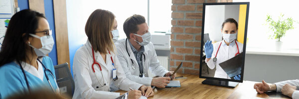 Медицинский персонал сидит за столом с документами и смотрит на монитор, на котором доктор видит разговор.