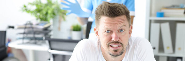 Young male patient lies on couch on stomach with doctor wearing rubber glove in background