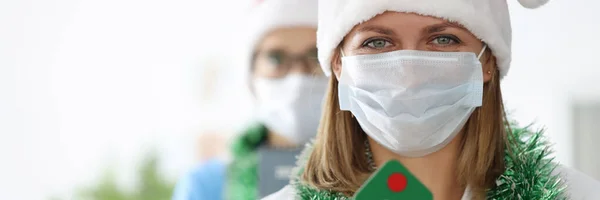 Jovens médicas em santa claus chapéus e ouropel em torno de seus pescoços estão segurando brinquedo árvore de natal — Fotografia de Stock