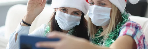 Duas mulheres em máscara protetora e santa claus chapéu falar on-line no telefone. — Fotografia de Stock
