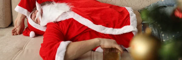 П'яний Санта Клаус спить на дивані з пляшкою віскі в руках вдома — стокове фото