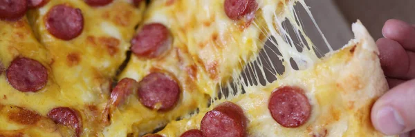 Male hands tearing off slice of pizza with cheese and sausage close-up — Stock Photo, Image