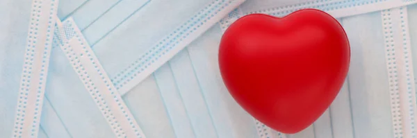 클리닉의 의료용 보호 마스크 사이 탁자 위에 누워 있는 붉은 장난감 심장 — 스톡 사진