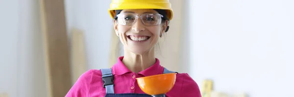 Mulher sorridente em chapéu amarelo duro e óculos segurando êmbolo na mão — Fotografia de Stock