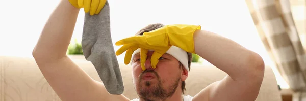 Опухший холостяк нюхает вонючие носки во время уборки — стоковое фото