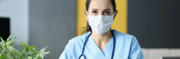 Doctor with protective medical mask siting at table in office and writing in documents