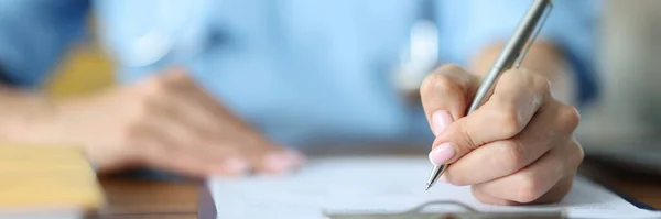 Γιατρός κρατώντας στο χέρι ασημένια πένα σε έγγραφα στο τραπέζι στο γραφείο close-up — Φωτογραφία Αρχείου