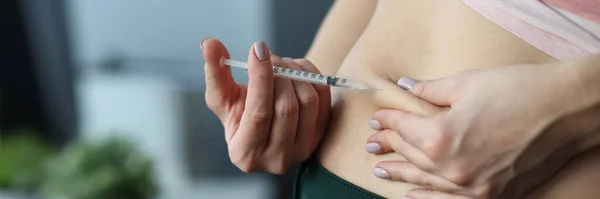 Woman making skin fold on stomach and injecting medicine from syringe at home