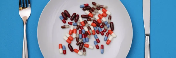 Lots of multi-colored capsule and lying on plate with fork and knife closeup — Stock Photo, Image