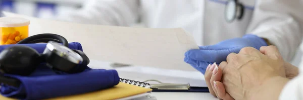 Médico sosteniendo cardiograma en guantes en las manos y asesorando al paciente en el primer plano de la clínica —  Fotos de Stock