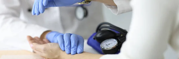 Orvos gumikesztyűben méri a betegek pulzusát és nézi az óráját a klinikán közelkép — Stock Fotó