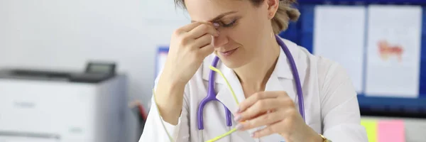 Cansado médico sentado à mesa em seu escritório e cuida de seus olhos — Fotografia de Stock