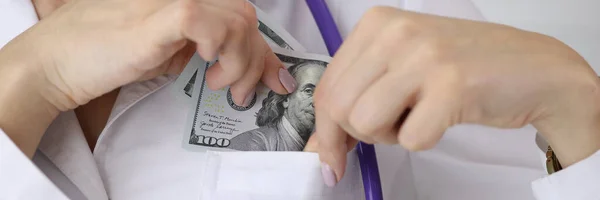 Médico colocando nota de dólar no bolso uniforme no closeup clínica — Fotografia de Stock
