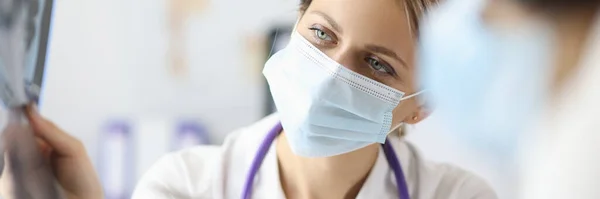 Dokter in beschermend medisch masker toont pen op röntgenfoto in kliniek — Stockfoto