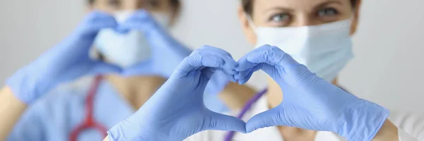 Deux médecins portant des masques médicaux et des gants en caoutchouc montrant le cœur avec leurs mains — Photo