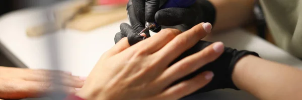 Profesjonalny w czarnych rękawiczkach zrobić zmechanizowany manicure dla odwiedzających w studio. — Zdjęcie stockowe