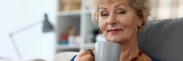 Nonna bere caffè e leggere libro in appartamento. — Foto Stock