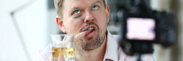 Zerzauster Mann hält Glas Alkohol in der Hand und schmeckt es mit dem Finger. — Stockfoto