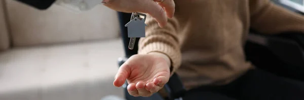 Vrouwelijke hand hold geven sleutel met sleutelhanger van nieuw huis en geven aan gehandicapten. — Stockfoto