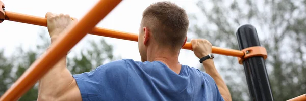 Hombre en azul camiseta tire de sí mismo en horizontal bar en parque. —  Fotos de Stock