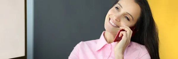 Молодая улыбающаяся женщина разговаривает по мобильному телефону за столом в офисе — стоковое фото