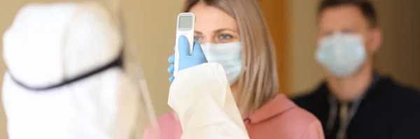 Doctor in protective suit measuring temperature of people in line with non-contact infrared thermometer — Stock Photo, Image