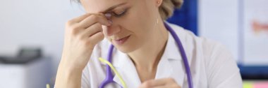 Elinde gözlüklerle klinikte gözlerini tutan yorgun bir doktor.