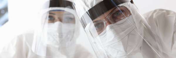 Нижний вид врачей в противочумных защитных костюмах и экранах в больнице