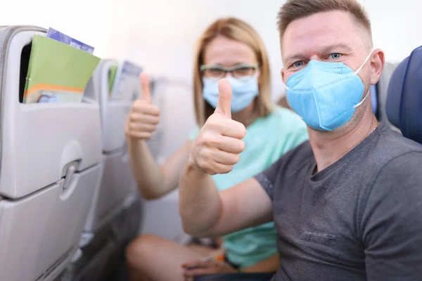 Mannen och kvinnan i medicinska skyddsmasker i flygplanskabinen håller tummarna upp — Stockfoto