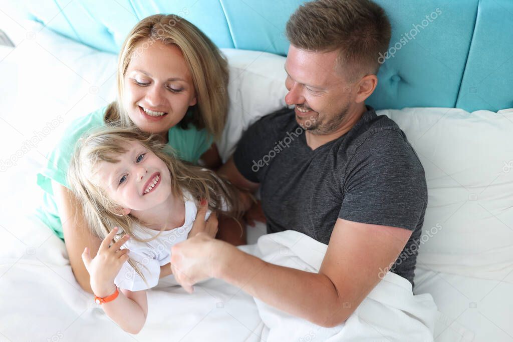 Parents with child indulge and cuddle in bed