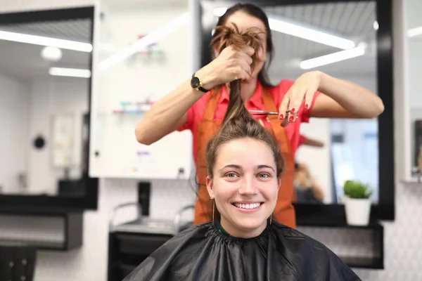 Portret uśmiechniętej kobiety w salonie fryzjerskim, której mistrz obcina włosy — Zdjęcie stockowe
