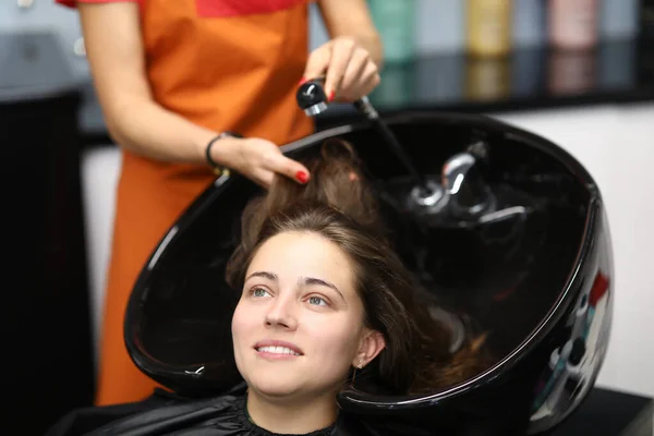 Mistr umývá její vlasy v umyvadle pro klienta v kadeřnictví — Stock fotografie