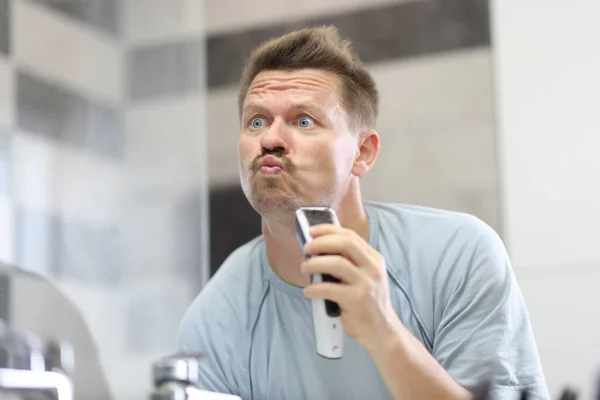 Man in front of a mirror shaves off his stubble with machine — Stock Photo, Image